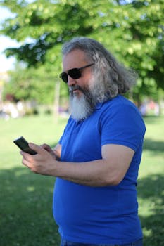 A senior man with sunglasses using a smartphone in a sunny park scene.
