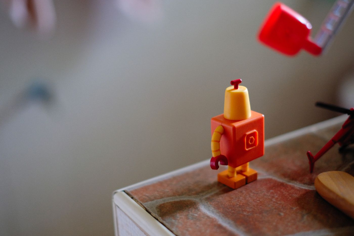 Close-up of a small colorful robot toy standing on a brown surface indoors.