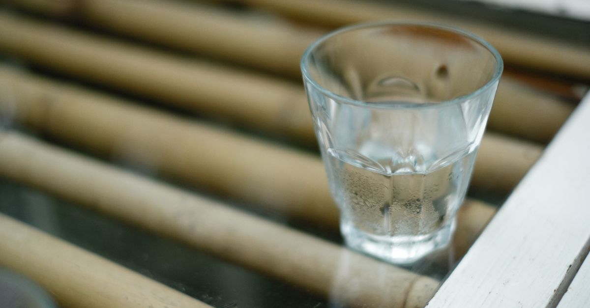Um copo de shot com líquido transparente colocado sobre uma superfície de bambu, criando uma cena reflexiva e tranquila.