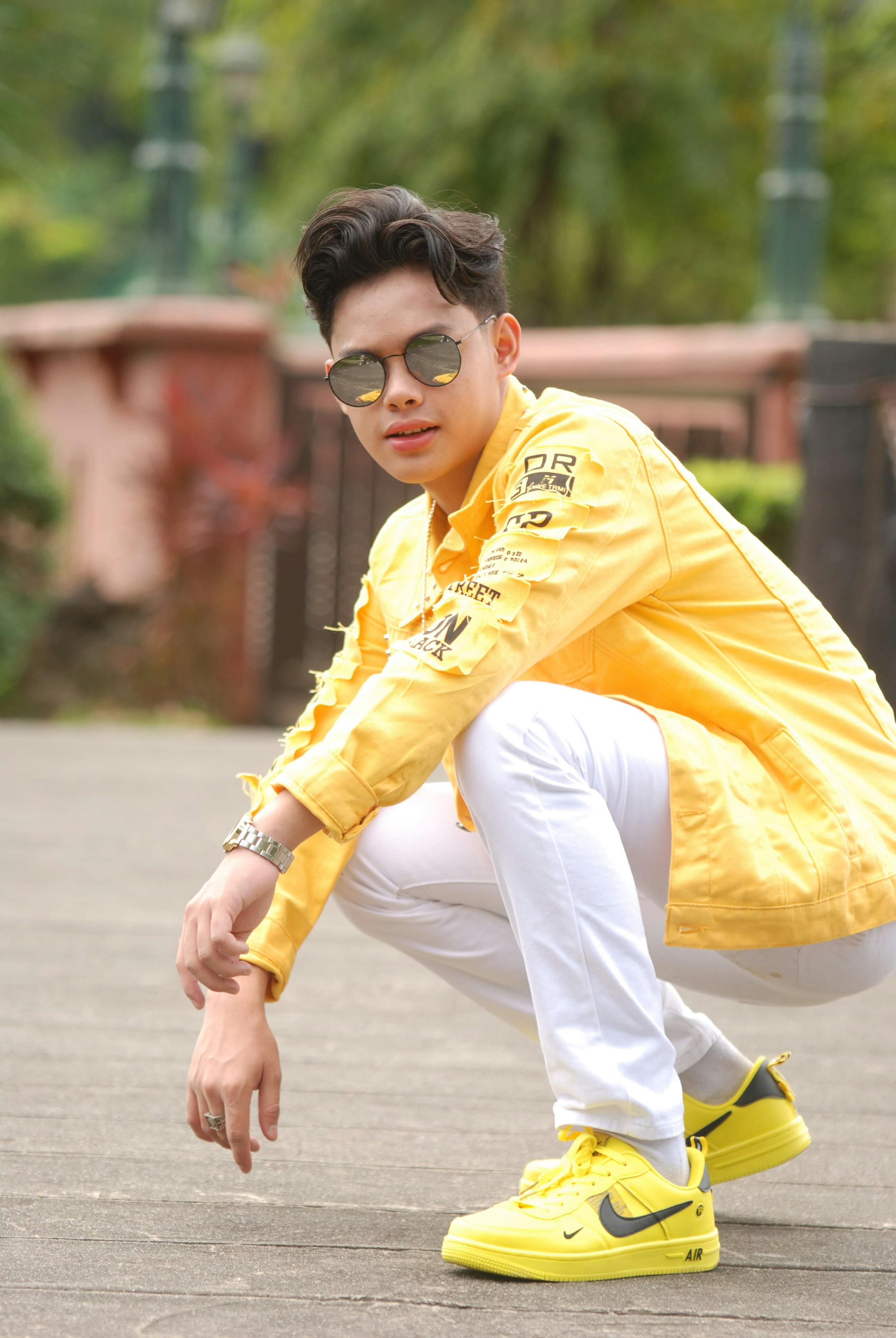 Stylish young man in yellow squatting outdoors, wearing sunglasses and Nike sneakers.