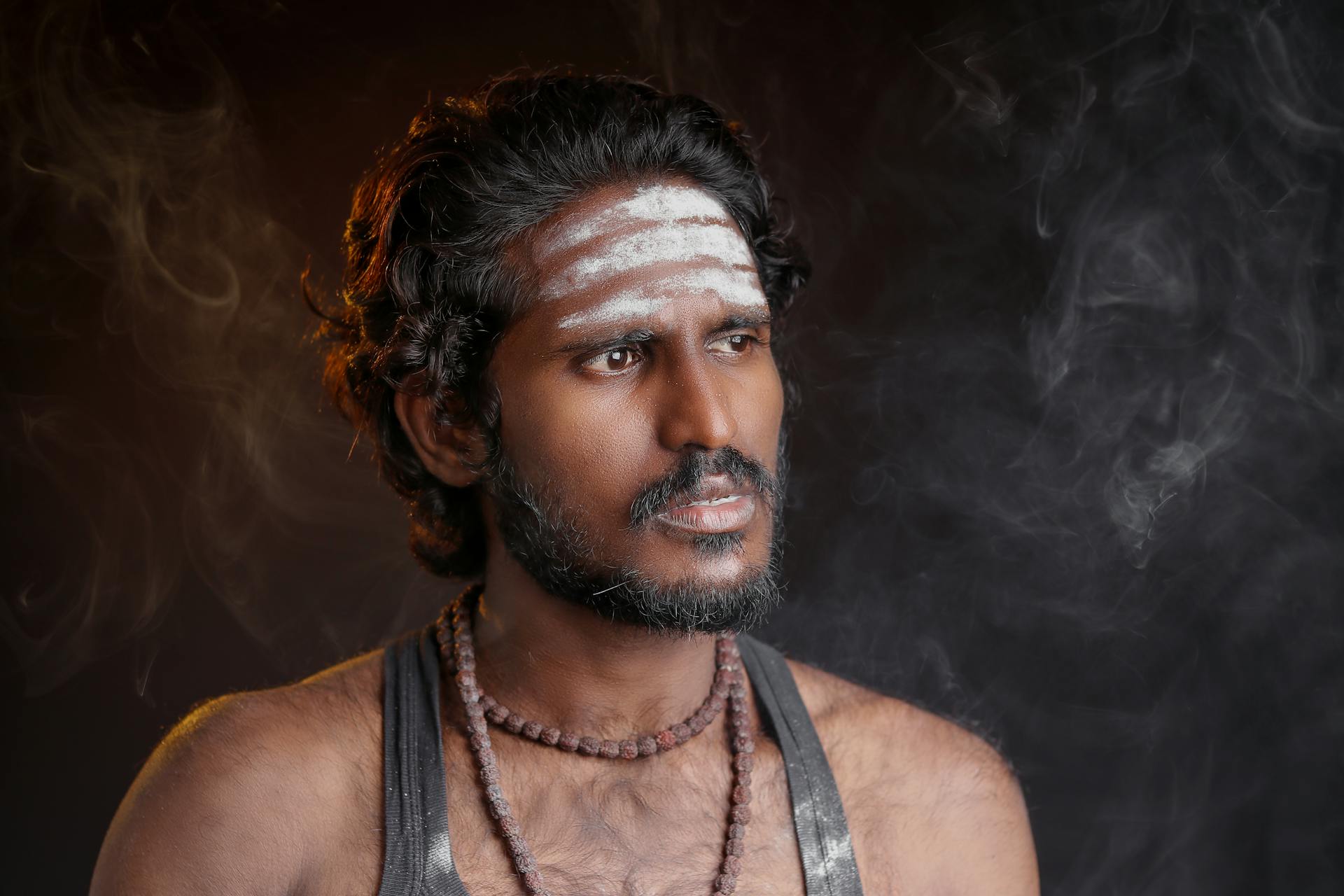 Close-up portrait of a man with traditional markings and smoke in Chennai studio.