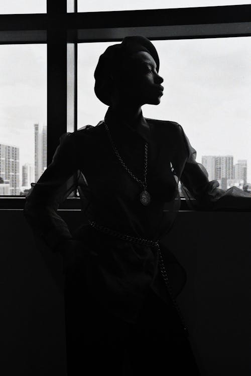 

A Grayscale of a Woman Leaning on a Window