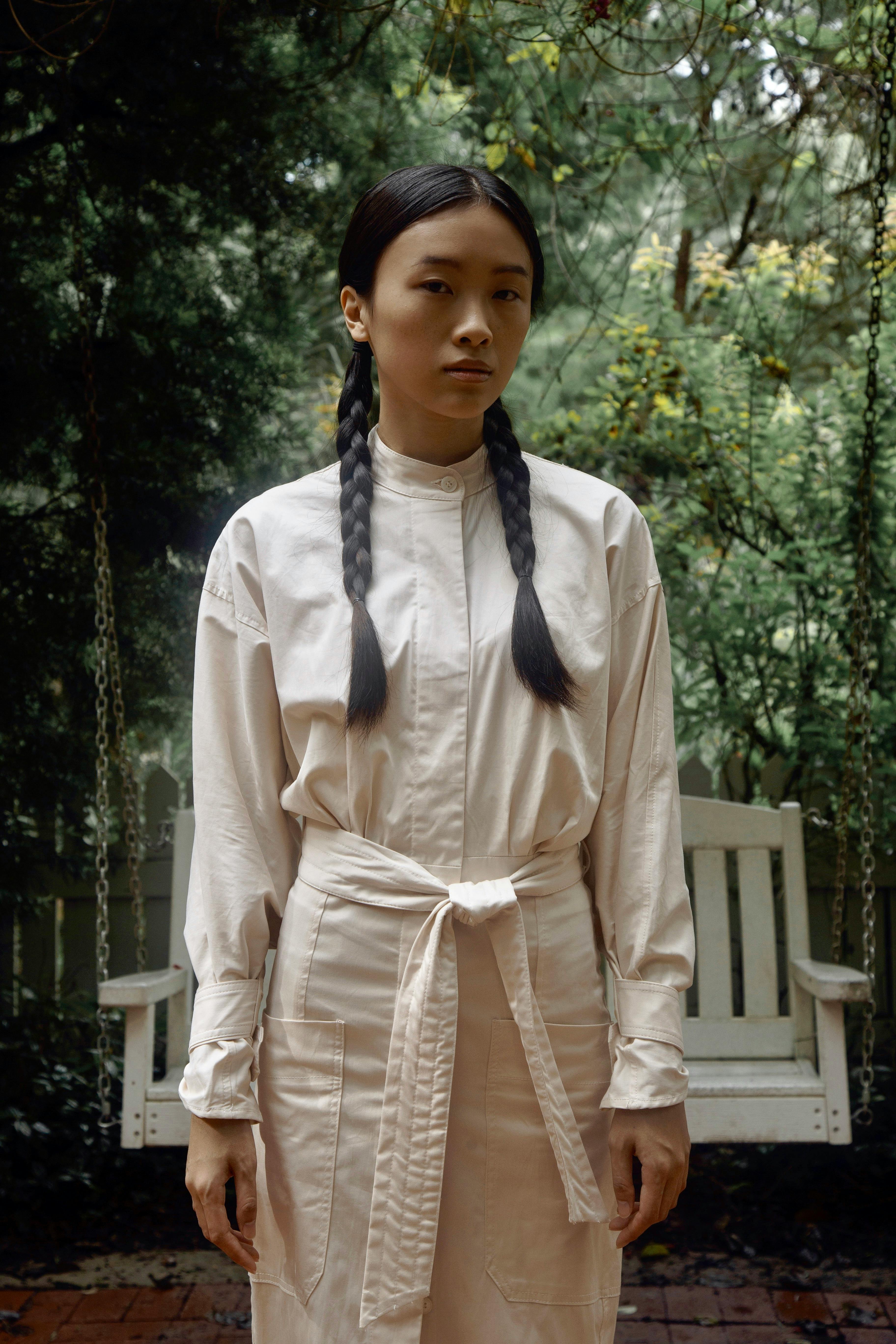 Woman with braids in white attire posing outdoors by a swing.