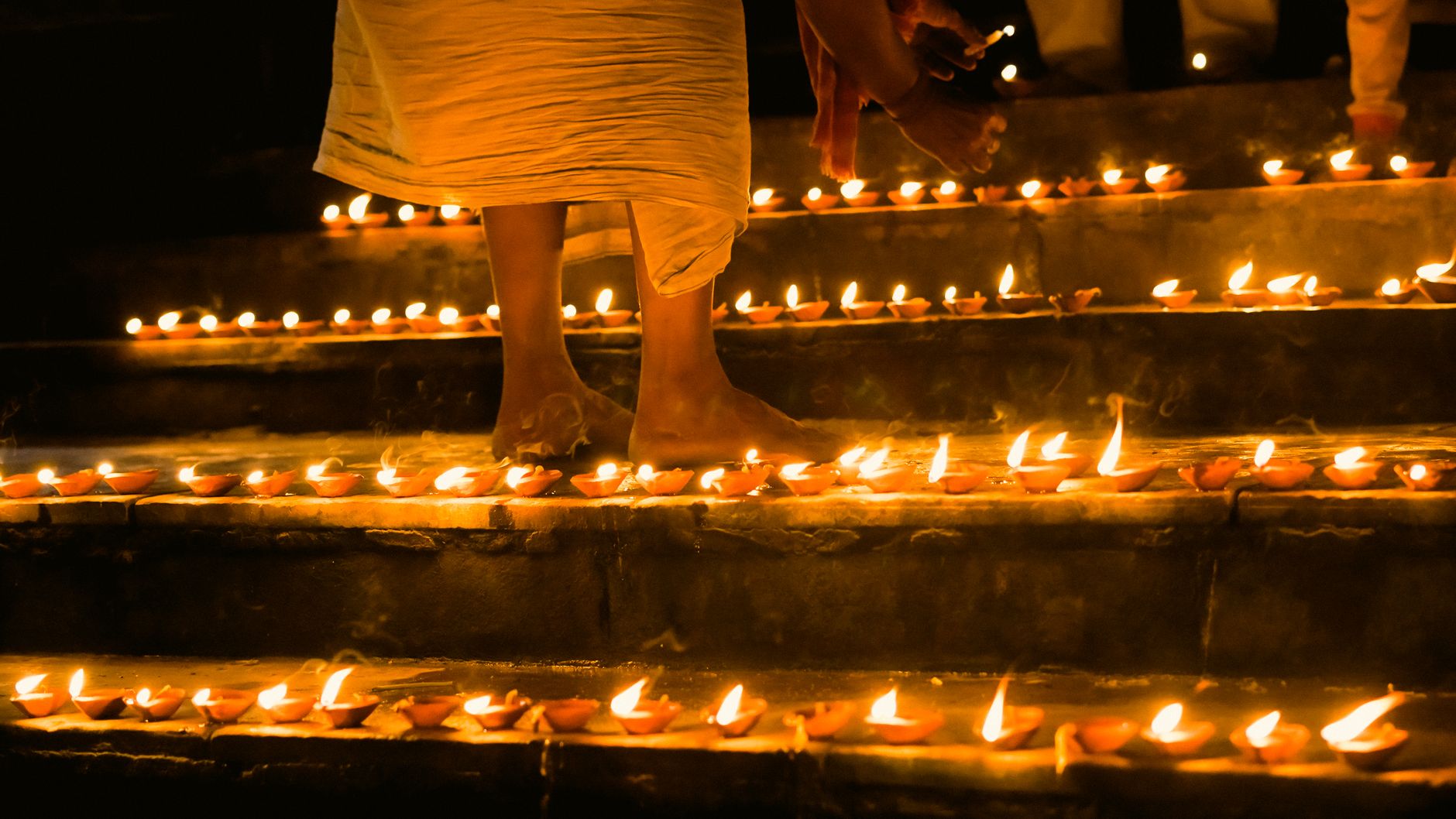 Barefoot figure navigating lit stairs during a nighttime candle ceremony.