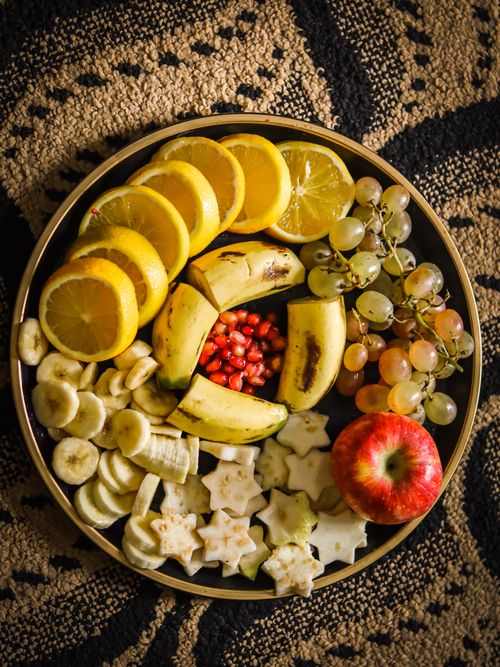 Free Vibrant selection of sliced fruits including apple, banana, lemons, and grapes arranged on a round decorative tray. Stock Photo
