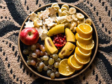 Colorful fruit platter with bananas, oranges, apple, grapes, and pomegranate on decorative background.