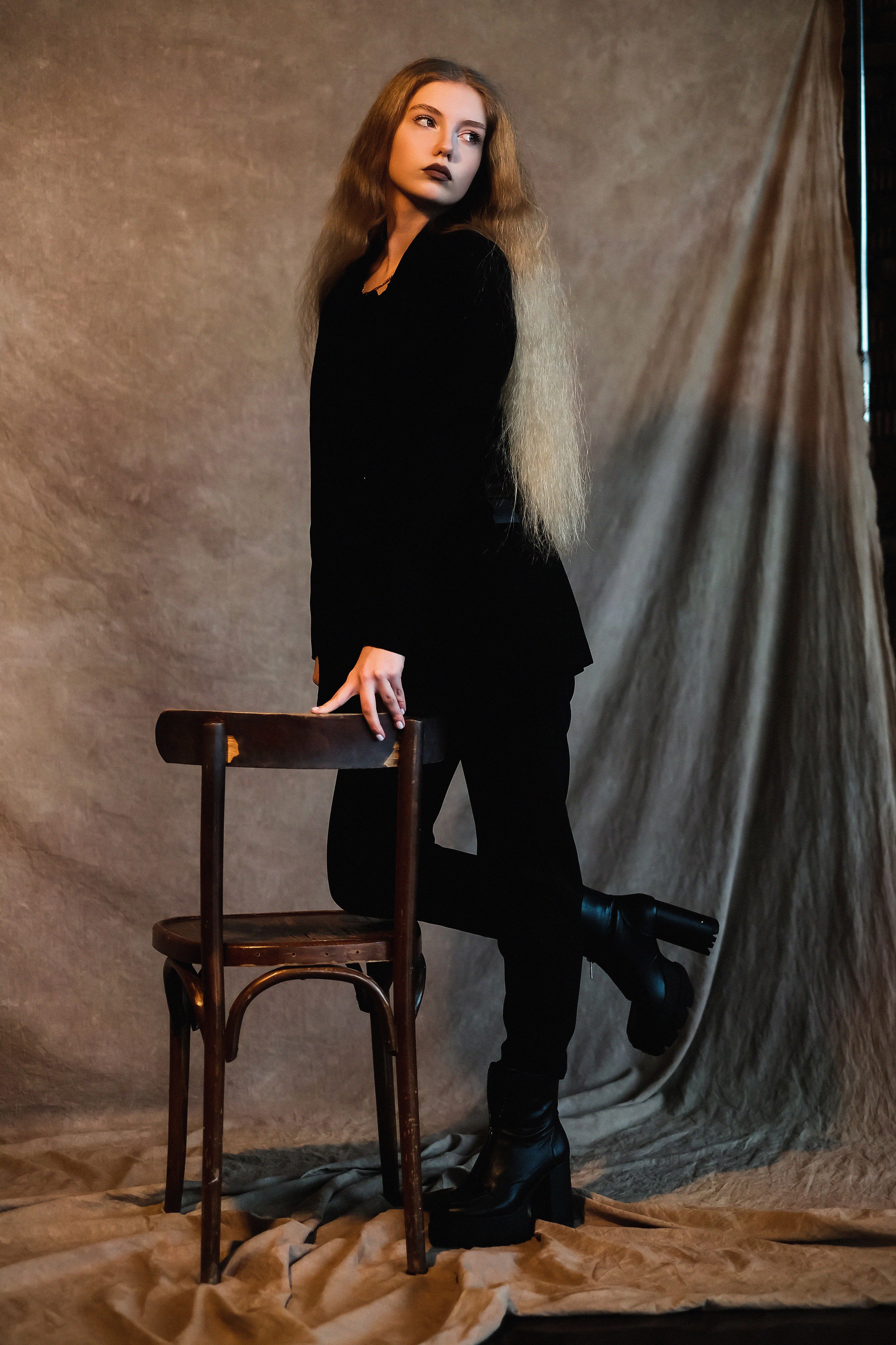 Woman in Black Coat Standing Beside a Brown Wooden Chair · Free Stock Photo