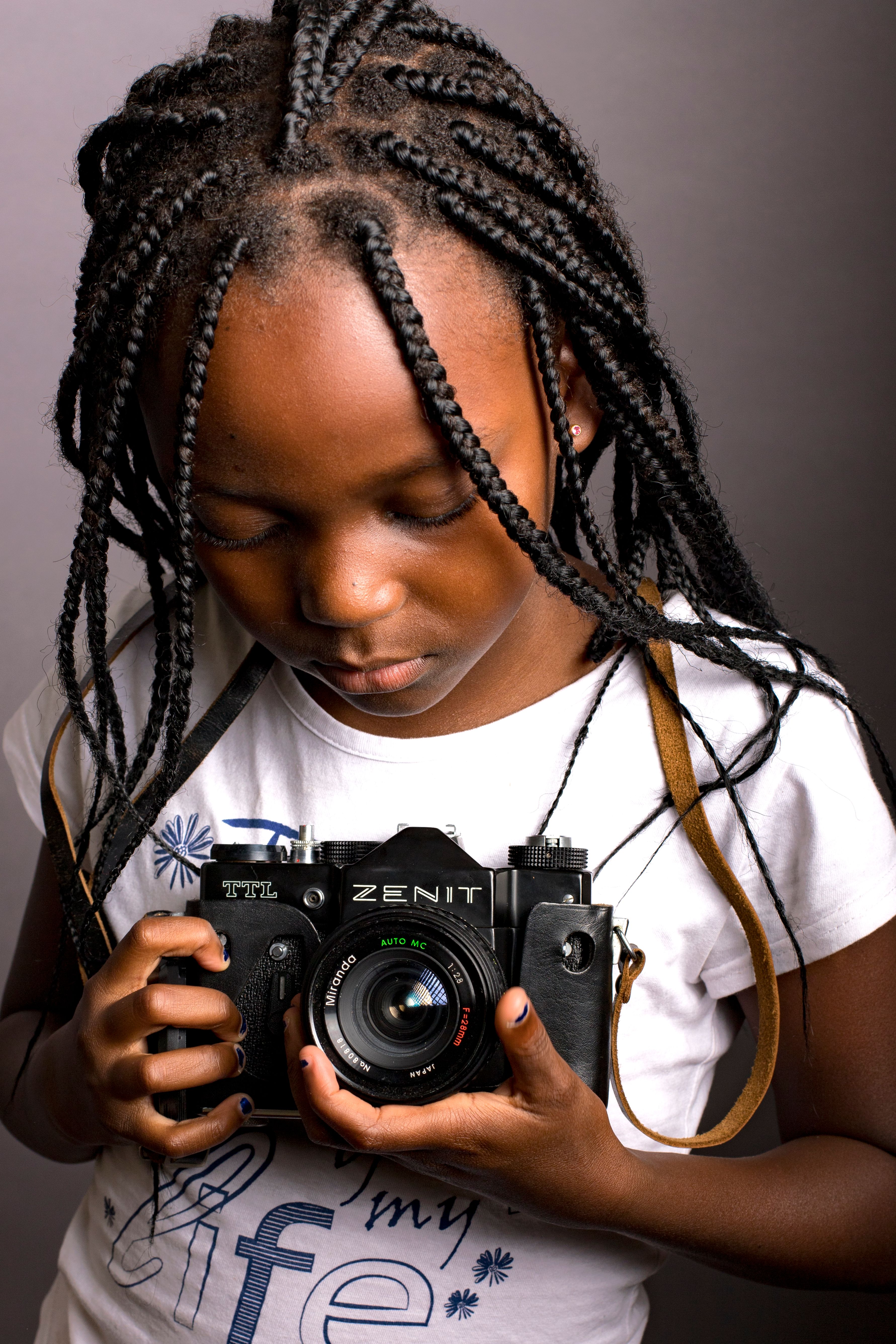 African American girl holding a vintage camera, showcasing braided hair style.