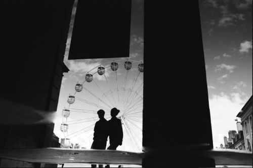 Free A dramatic black and white silhouette of a couple standing near a Ferris wheel during dusk. Stock Photo