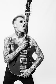 Tattooed musician passionately posing with electric guitar in artistic black and white photo.