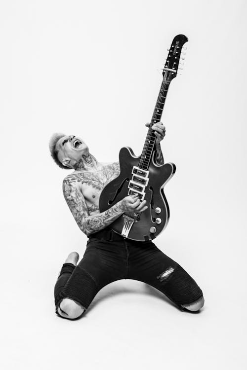 
A Grayscale of a Tattooed Man Playing the Guitar