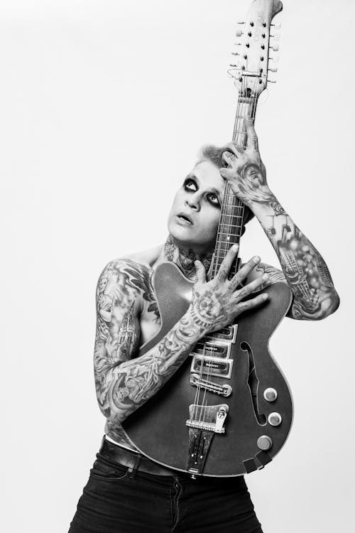 A Grayscale of a Tattooed Man Holding a Guitar