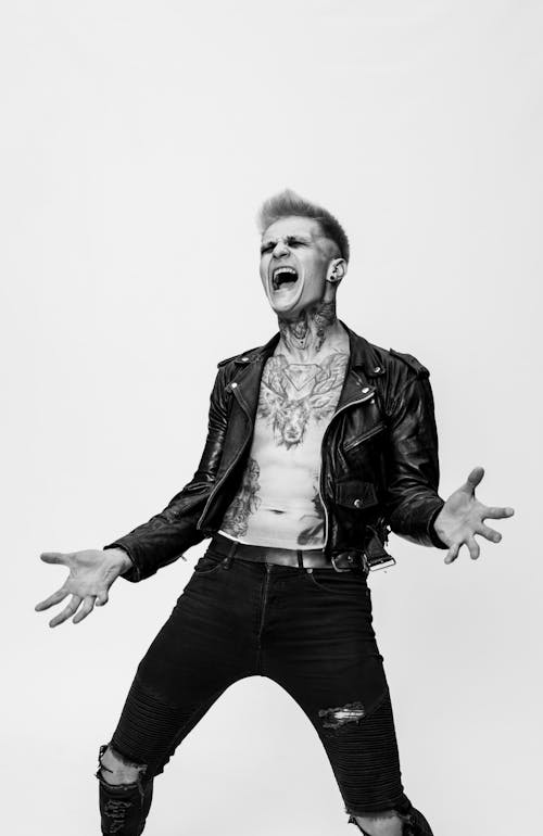 A Grayscale of a Tattooed Man Wearing a Leather Jacket Screaming