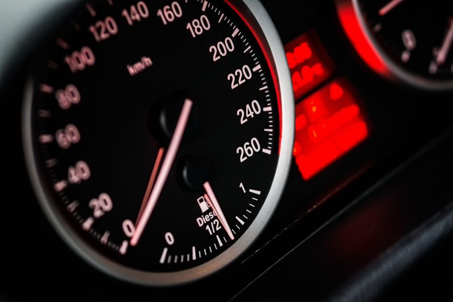Detailed view of car speedometer and odometer with illuminated red gauges.