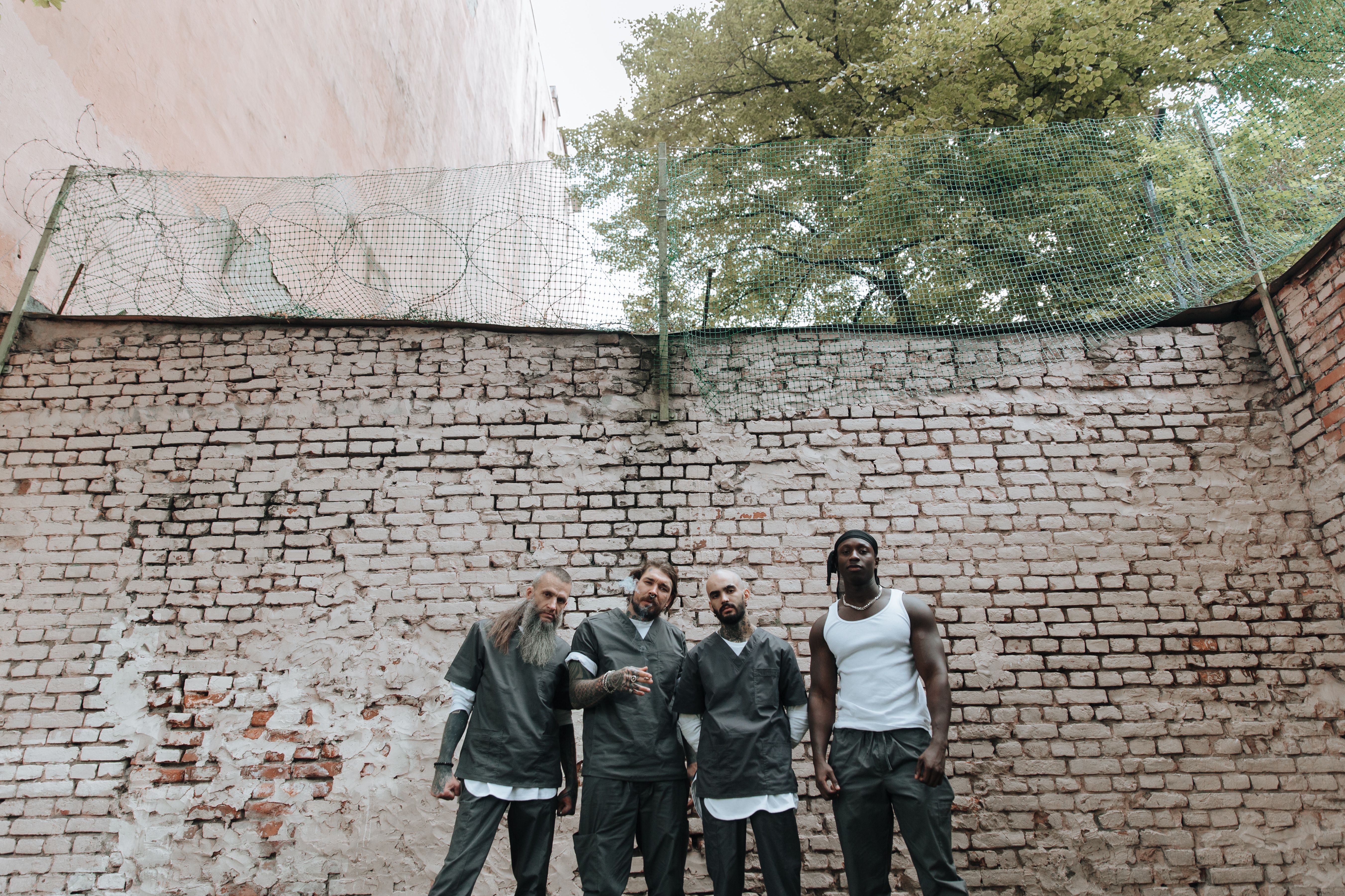 Four diverse men stand confidently against a brick wall in an outdoor setting.