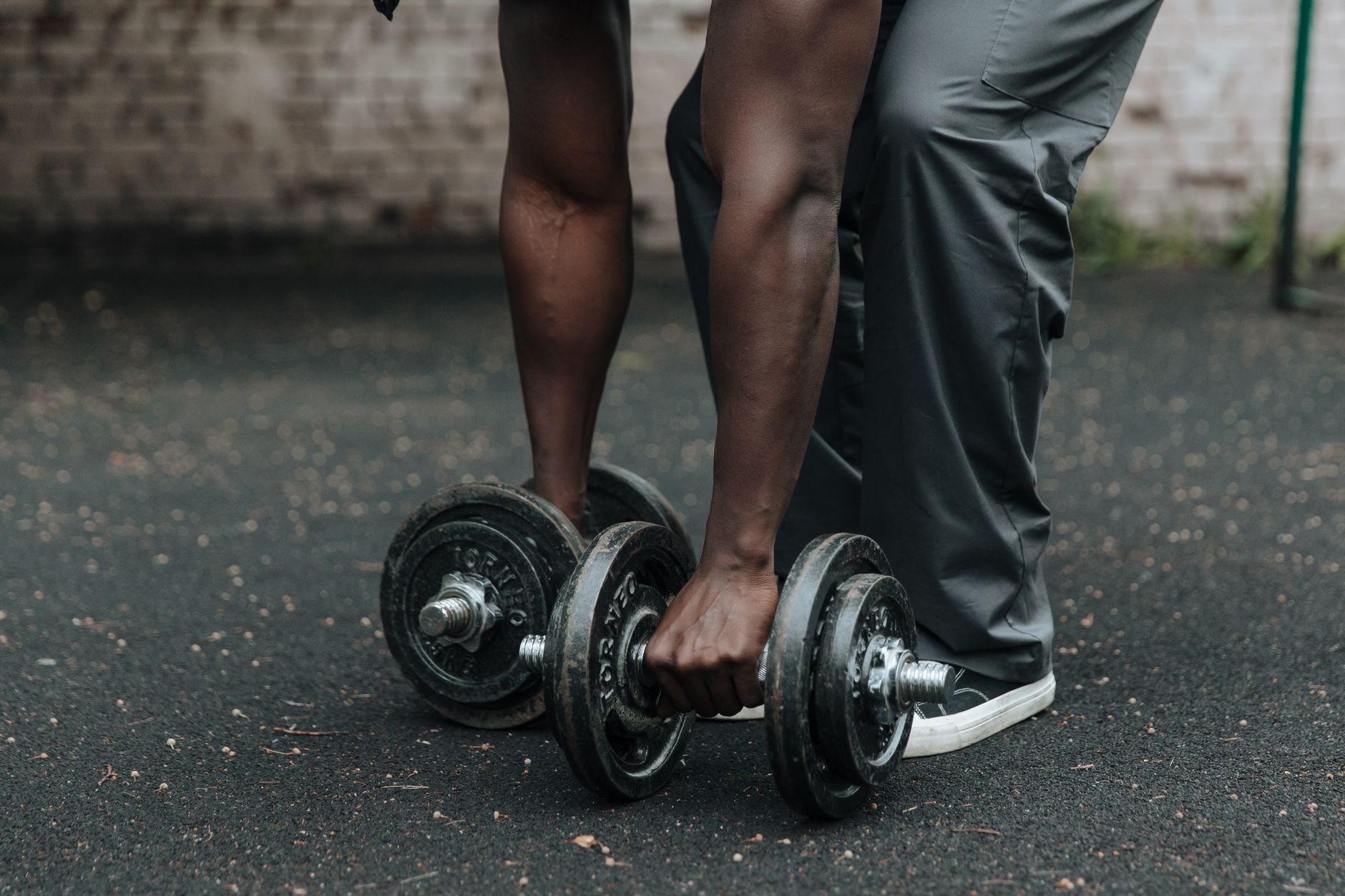 A fit man lifting heavy dumbbells outdoors, focusing on strength training and muscle building.