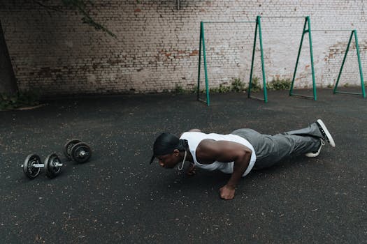 A man in sports attire doing push-ups on an outdoor asphalt surface beside dumbbells.