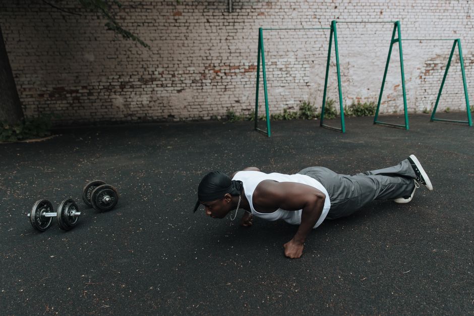 A man in sports attire doing push-ups on an outdoor asphalt surface beside dumbbells.