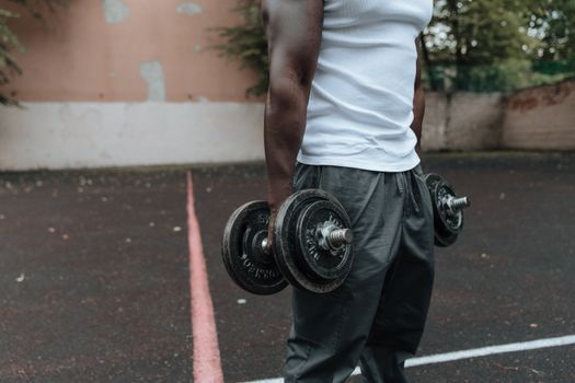 Athletic man holding dumbbells in an outdoor workout setting, showcasing strength and fitness.