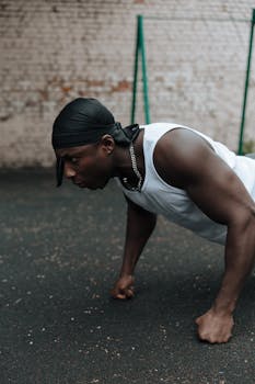 Man wearing headband performs push-ups outdoors on gritty surface.