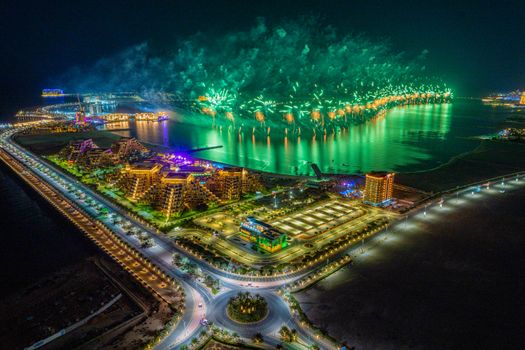 A breathtaking aerial view of fireworks illuminating Ras Al Khaimah's cityscape, showcasing vibrant lights over water at night.