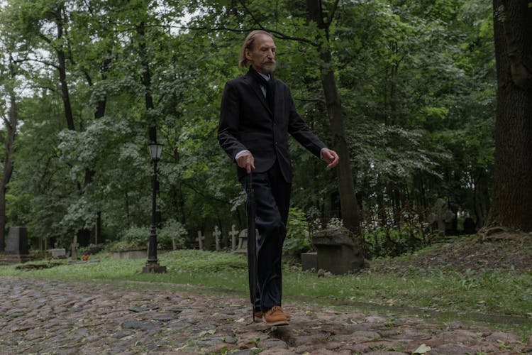 Man In Black Outfit Walking On Rocky Pathway With A Cane