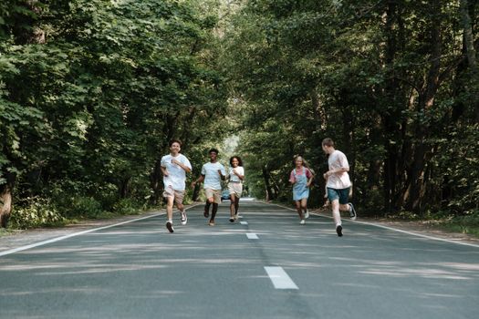 A group of teenagers running with joy on a tree-lined road on a summer day.