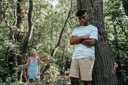 Boy Leaning Against Tree with Girl Standing in Background