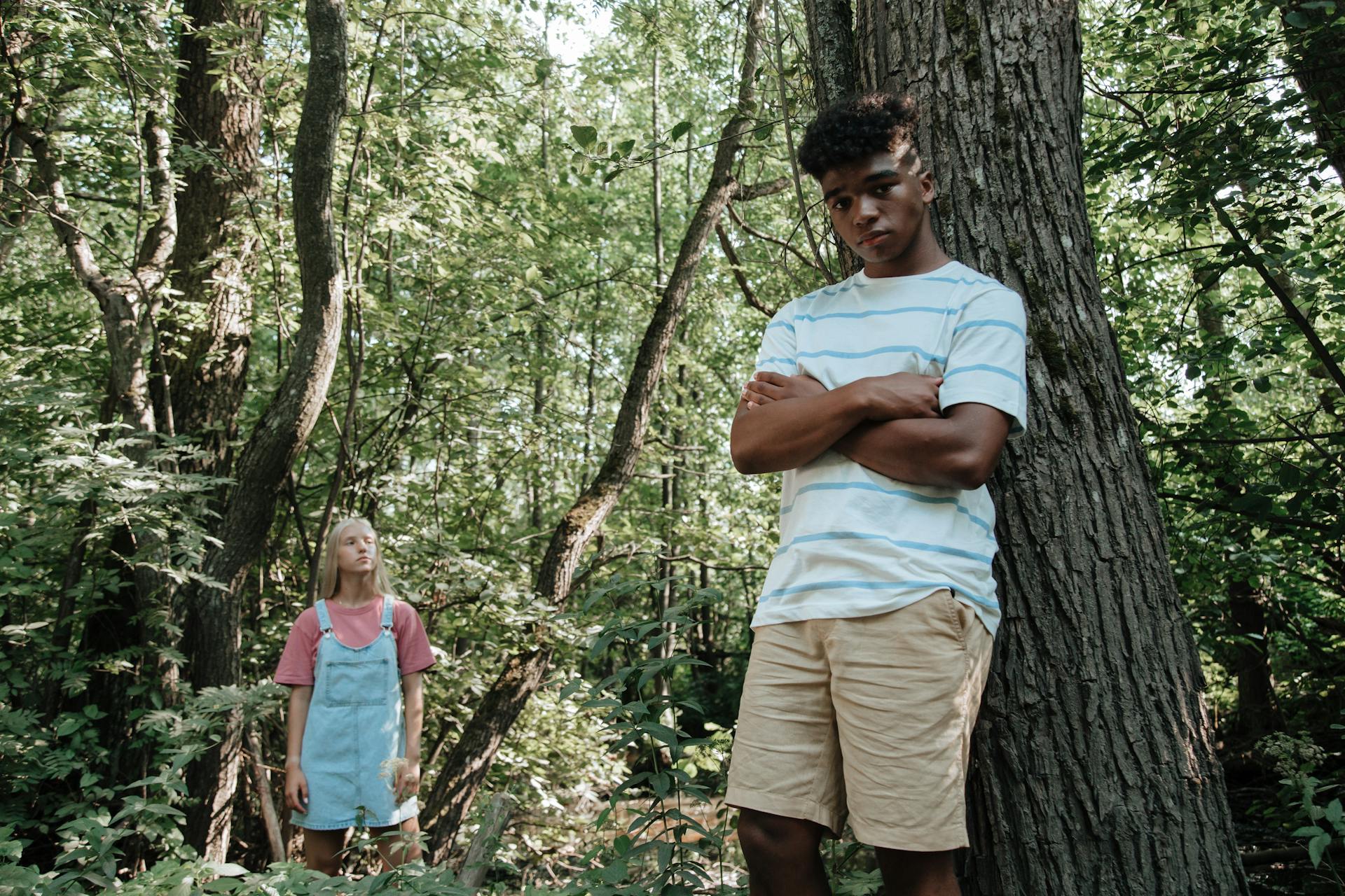 Boy Leaning Against Tree with Girl Standing in Background