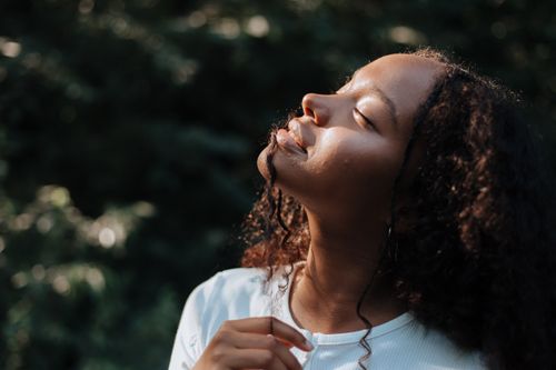 Free A serene portrait of an African American woman enjoying sunlight in a forest setting. Stock Photo