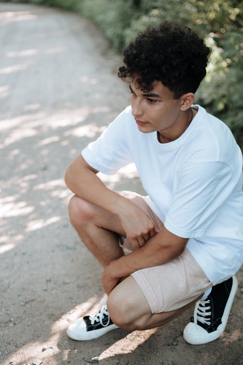 Free Teenage Boy in Bright Summer Outfit Crouching on Footpath Stock Photo