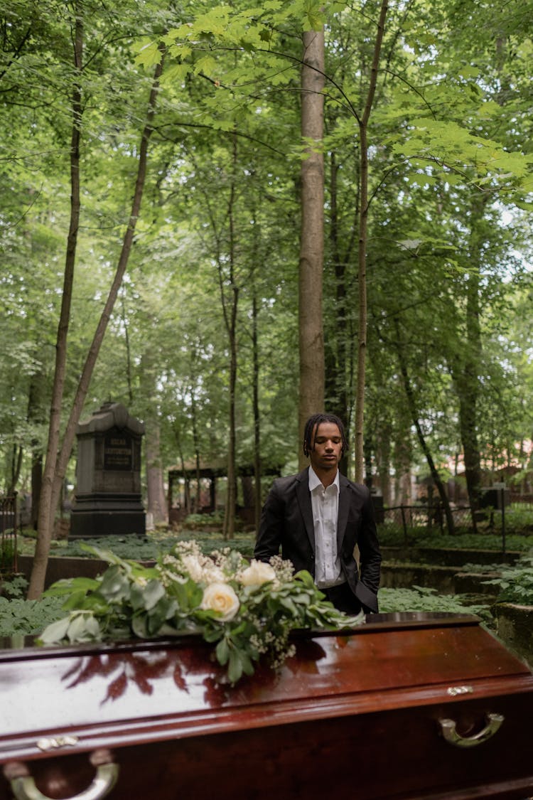 A Man In Black Suit Standing In Front Of The Coffin