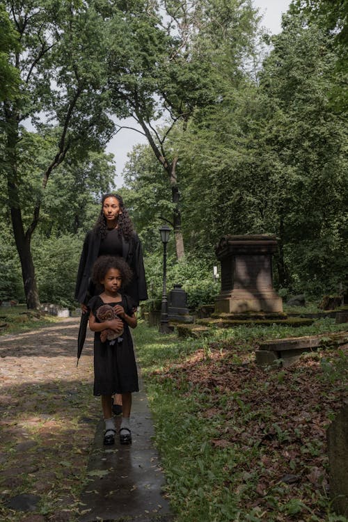 A Woman and a Young Girl in Black Clothes Standing in Cemetery