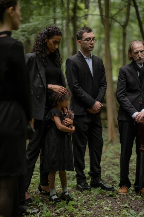 Free A group of mourners stand solemnly in a forest during a funeral. Stock Photo