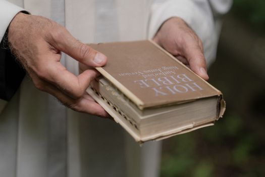 An elderly person gently holds a well-worn Holy Bible in their hands.