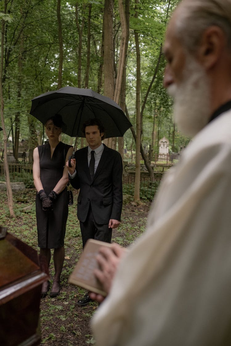 Man Holding A Black Umbrella Standing Beside The Woman In Black Dress