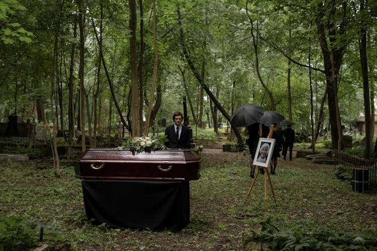 A Man In Black Suit Standing Near The Coffin 