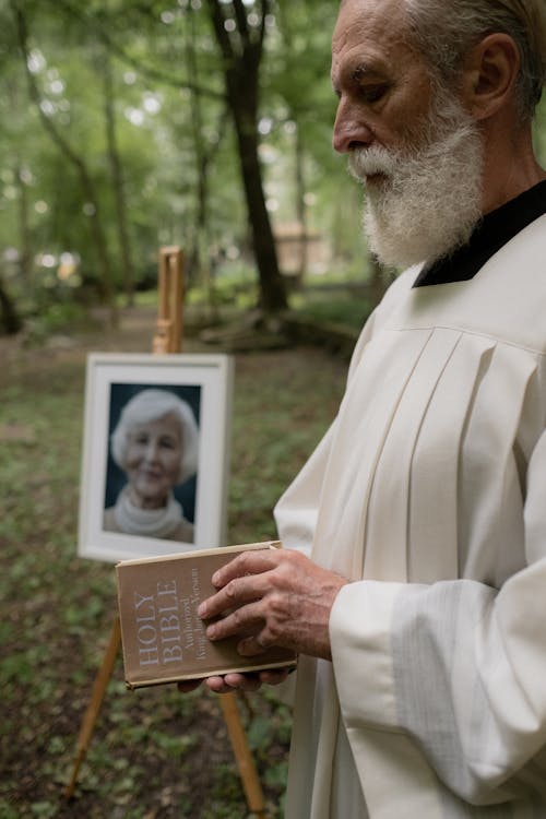 Priest with a Bible in His Hands Next to a Portrait of the Deceased