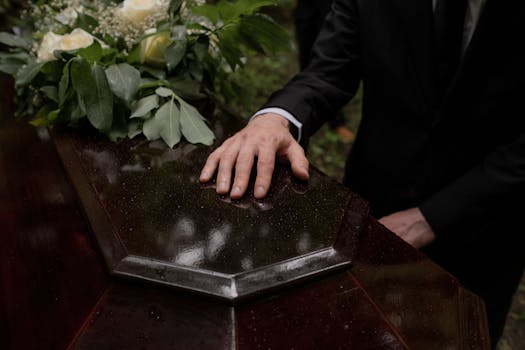 A hand placed on a coffin with flowers, symbolizing loss and mourning.