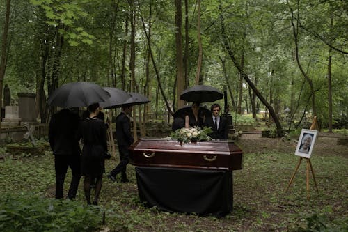 Brown Coffin Surrounded by People in Black Clothes 