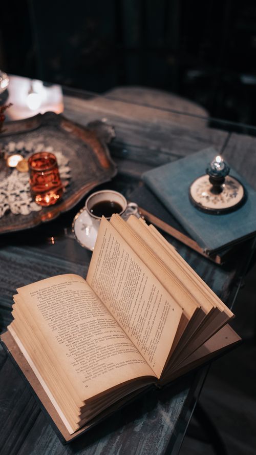 Free A cozy scene with an open book, cup of coffee, and candle on a rustic table, creating a warm atmosphere. Stock Photo
