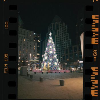 Illuminated Christmas tree in a bustling city plaza at night, surrounded by high-rise buildings.（イメージ）