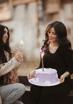 Two women celebrating with a lilac birthday cake and sparklers, radiating happiness and togetherness.