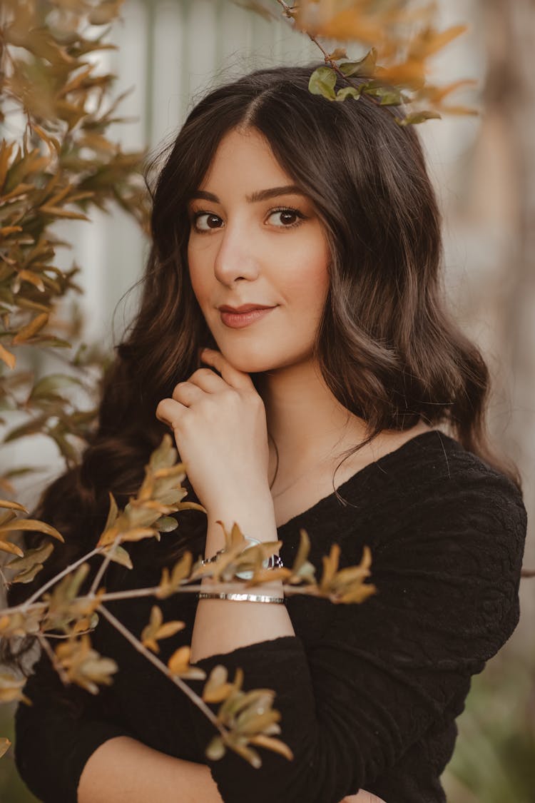 Brunette Beauty In Black Pullover Looking From Behind Plant With Yellow Leaves