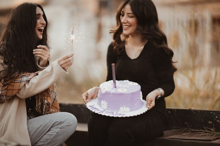 Two Lovely Women Sitting Outdoors With Birthday Cake And Sparkler