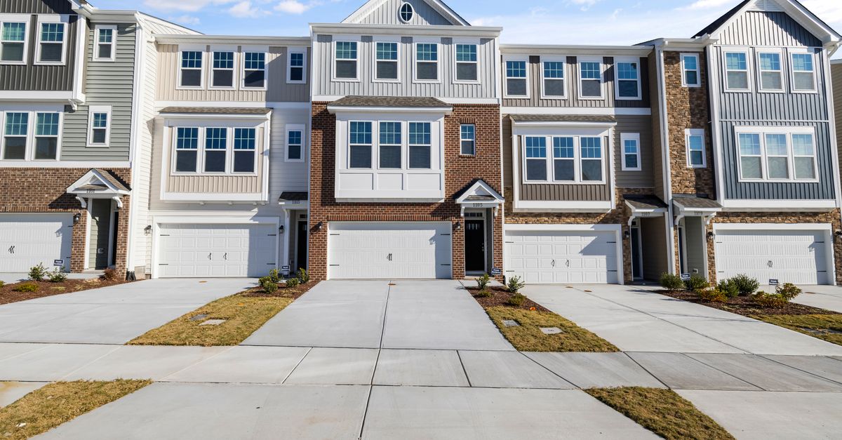 Row of modern townhouses with spacious driveways and garage fronts under blue sky.