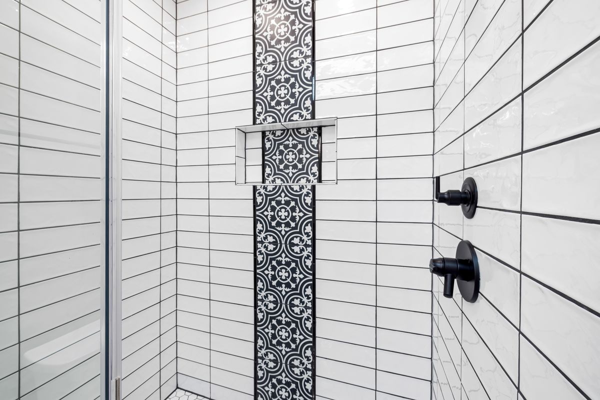 Modern shower area with white rectangular wall tiles, dark grout, patterned accent tiles and black fixtures.