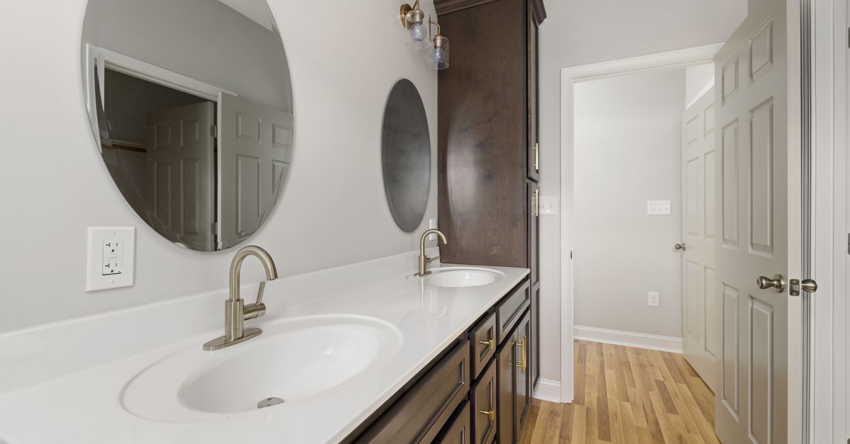A stylish bathroom interior featuring dual round mirrors, a double sink vanity, and wooden flooring.