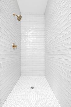 A clean, minimalist bathroom shower featuring white tiles and brass fixtures.