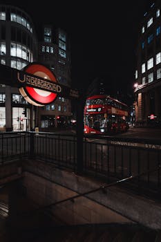 Night view of a London street with double-decker bus and Underground sign, capturing urban life.